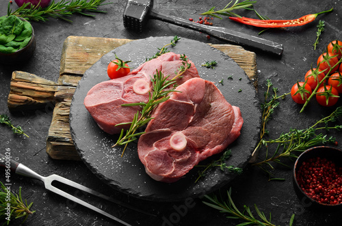 Meat. Lamb steak on the bone with rosemary and spices. On a black stone background. Top view. photo