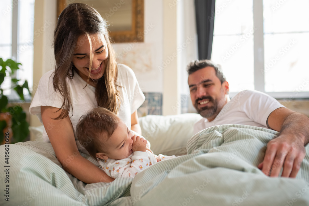 Cheerful woman playing with her baby son in bed. Happy parents lying in bed with child in morning. Family at home concept Cheerful woman playing with her baby son in bed. Happy parents lying in bed with child in morning. Family at home concept