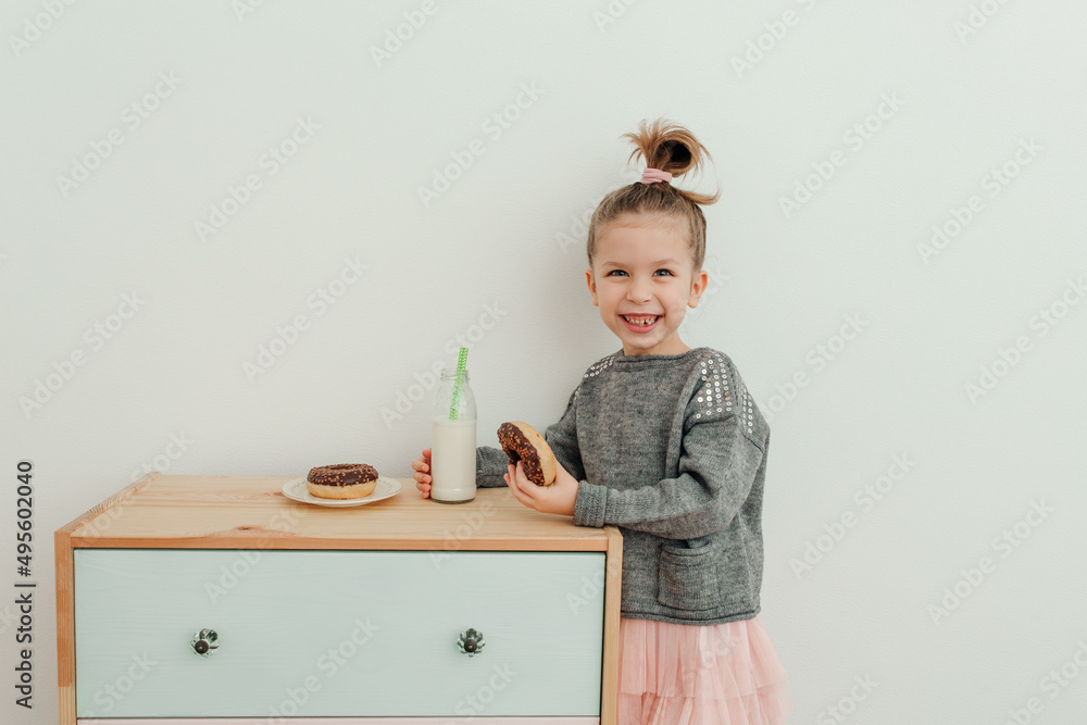 Lovely little girl is eating chocolate donut with bottle of milk. Portrait of cute stylish girl satisfied eating donuts. Sweets lover concept Lovely little girl is eating chocolate donut with bottle of milk. Portrait of cute stylish girl satisfied eating donuts. Sweets lover concept