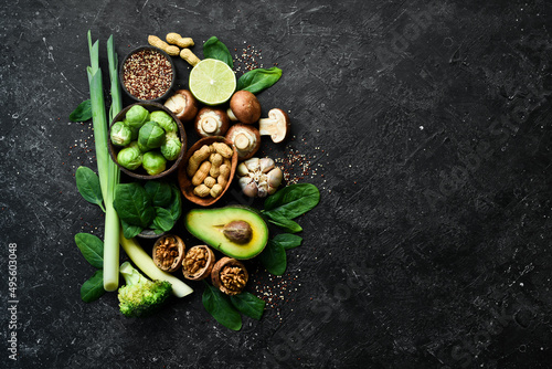 Healthy food set: Green vegetables, avocados, broccoli, nuts, mushrooms, berries and spinach. On a black stone background. Top view. Copy space.