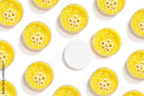 Bath salt sea with herbal extract of chamomile, natural sea salt crystals in round jar, decorated natural chamomile flowers. Pattern from spa product isolated on white, body care cosmetics