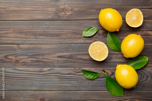 Many fresh ripe lemons with green leaves on colored background  top view  space for text