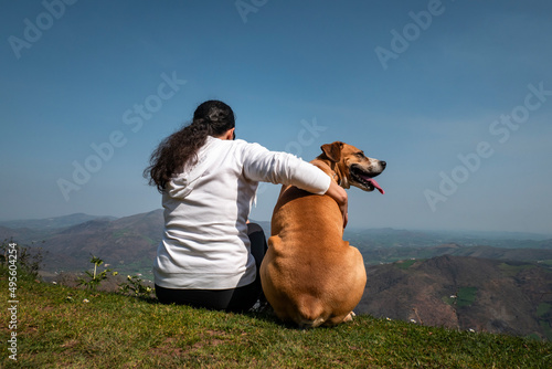 Mulher turista sentada a relaxar com seu cachorro enquanto aprecia as montanhas e aldeias ao fundo da montanha Jara em Irouléguy no País Basco photo
