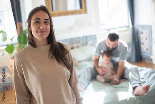 Portrait of happy young woman on background of husband and son at home. Mother looking at camera and smiling in bedroom. Family at home concept