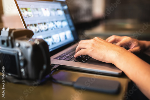 There is a photographer working on a laptop and related equipment on the table(soft focus image).