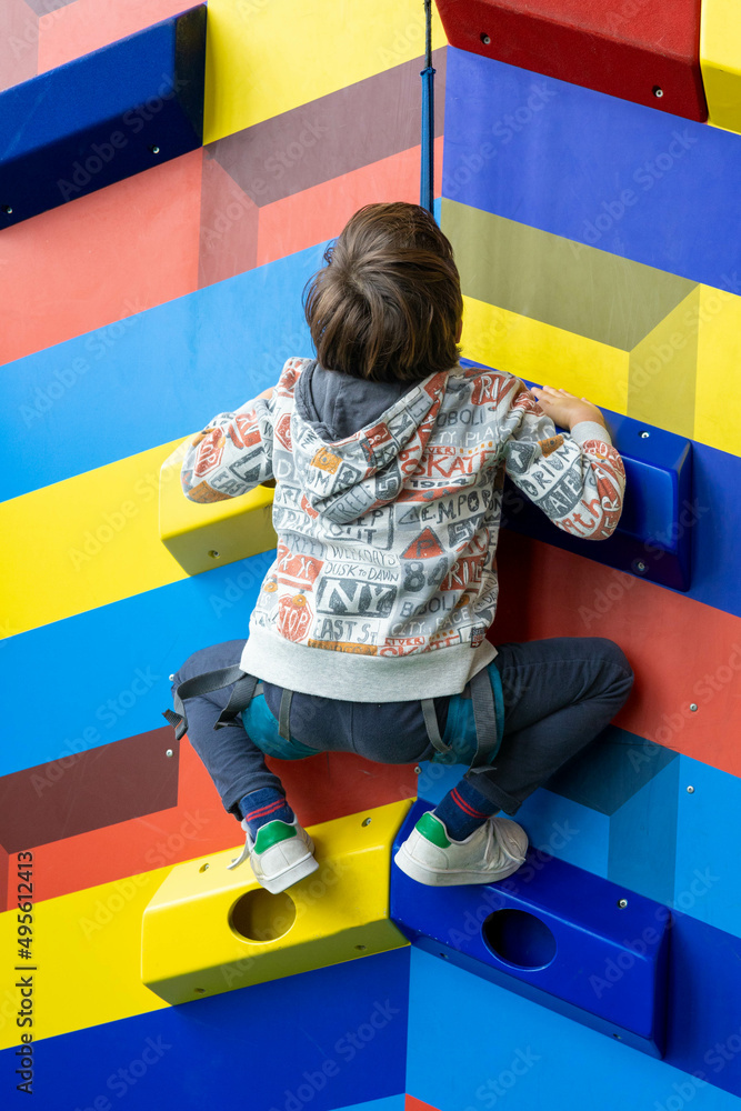 Child climbind a colorful wall with an harness for his security Child climbind a colorful wall with an harness for his security