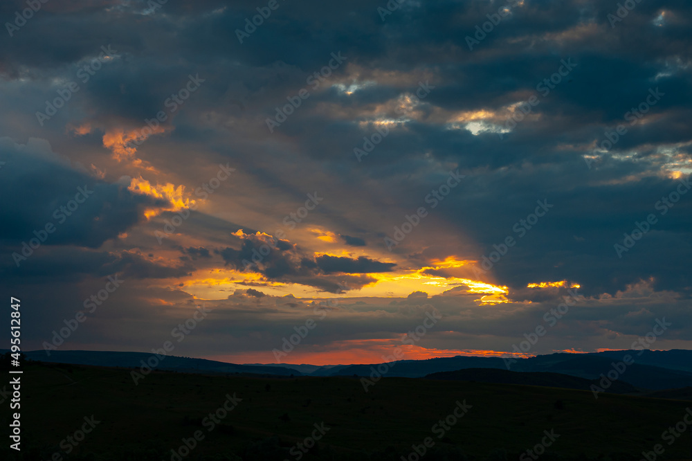 Amazing orange and blue sunset with rays of sun bursting from the clouds. Beautiful landscape from Transylvania, Romania. Amazing orange and blue sunset with rays of sun bursting from the clouds. Beautiful landscape from Transylvania, Romania.