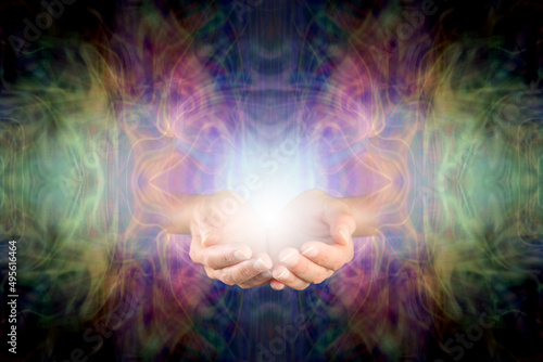 Darkness and Light Healing Hands - female cupped hands and white light orb emerging from a complex multicoloured ethereal energy field background with copy space all around 