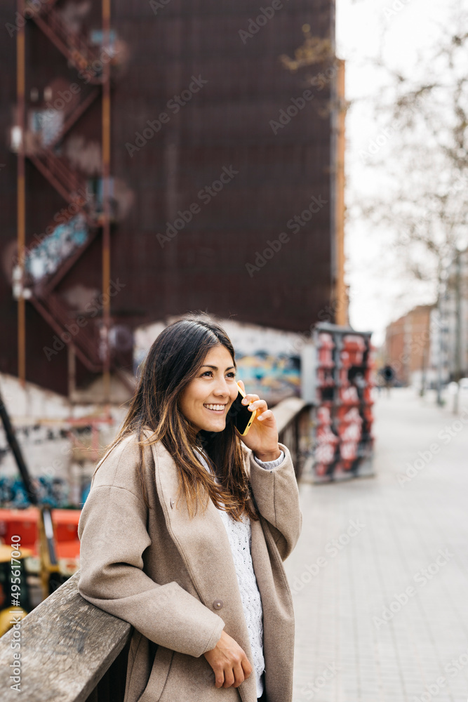 Portrait of a young smiling woman talking on a phone in the street