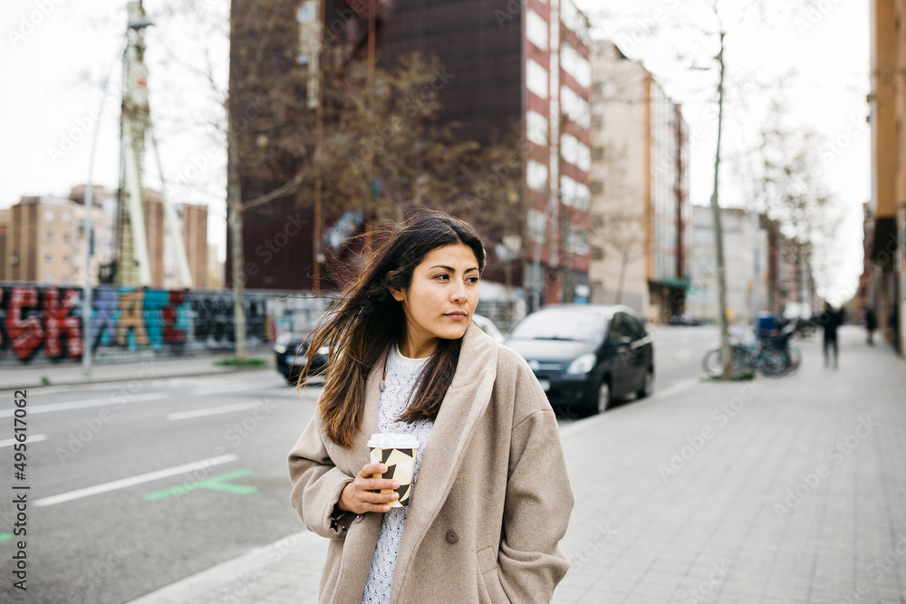Fototapeta premium Portrait of a young woman with a coffee cup walking on the street