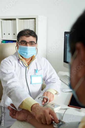General practitioner in medical mask measuring blood pressure of senior patient