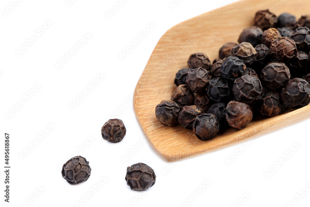 Fototapeta premium Close up of black pepper corns in a wooden spoon and scattered on white background.