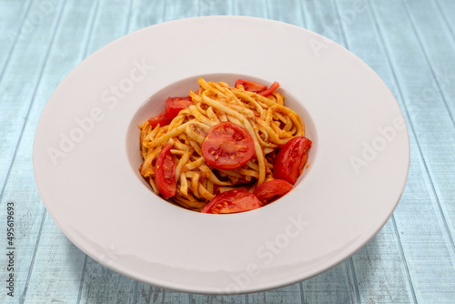Italian Bavette pasta with tomato sauce, parmesan and fresh cherry tomatoes in white plate on light blue wood table