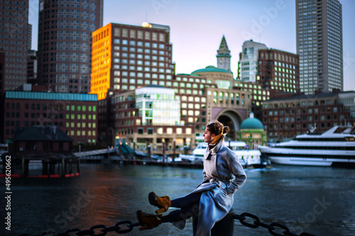 girl in coat against the backdrop of the cityscape yachts and riverboats moored in Boston harbor