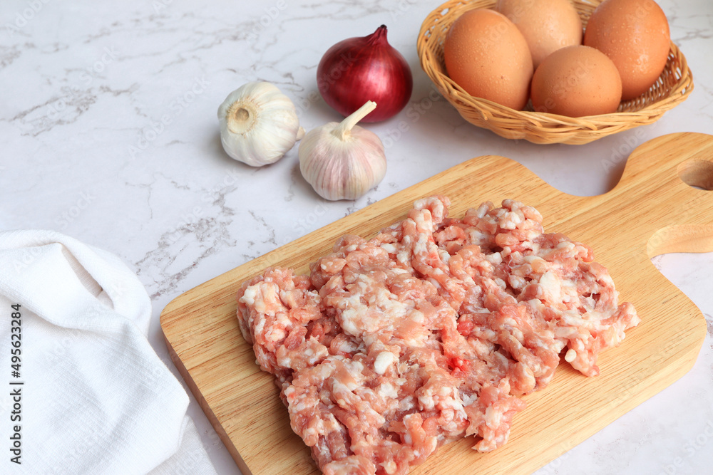 Raw pork meat, raw fresh minced meat on a wooden cutting board with ingredients for cooking on the table.
