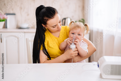 a little girl cries when inhaled with a nebulizer. A child with a viral disease in an inhalation mask is sitting in his mother's arms. Patient with asthma