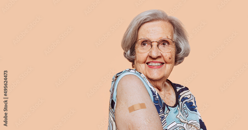 Portrait of a smiling elderly grandmother after receiving a vaccine. Elder woman showing her bandaged arm after receiving vaccination. - obrazy, fototapety, plakaty 