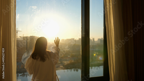 Woman Looks Out the window Touch the window With The Hand through the sun. Concept of thinking positive.