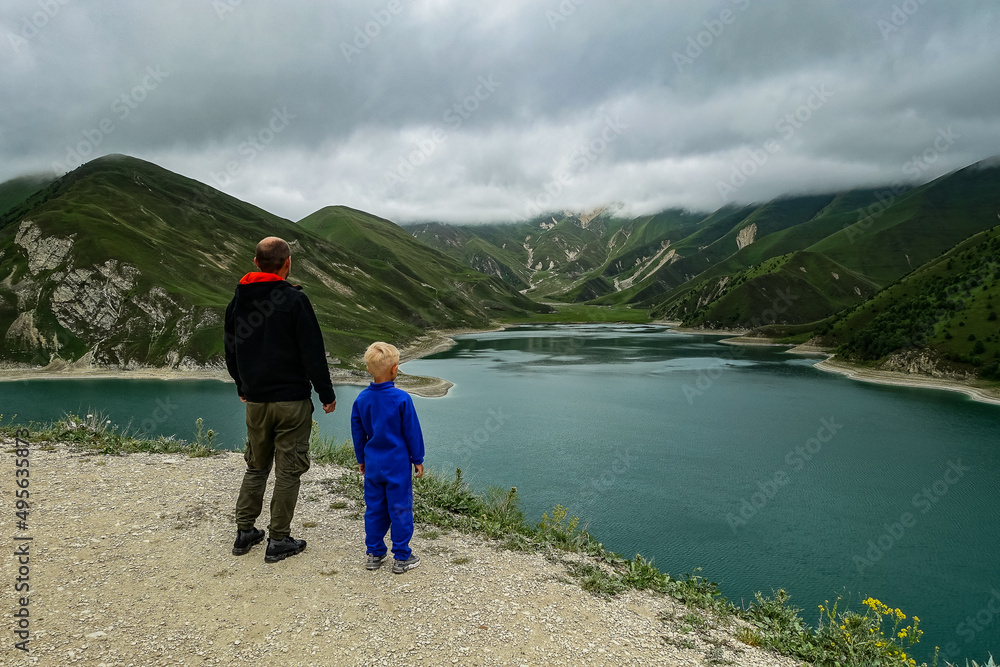 A man with a child on the background of Lake Kezenoy-am in the Caucasus mountains in Chechnya, Russia, June 2021.