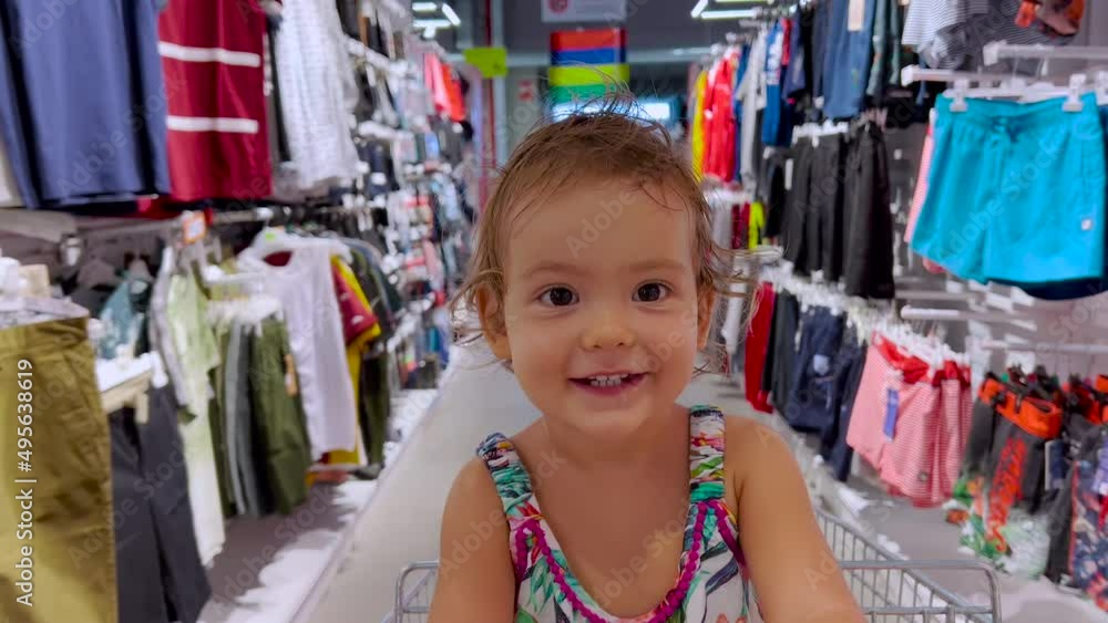 Baby rides in a shopping cart down a row in a supermarket. Little girl