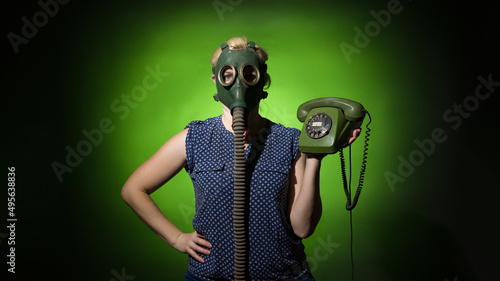 A woman in a gas mask holds a retro phone in her hand on a dark background, hard light.