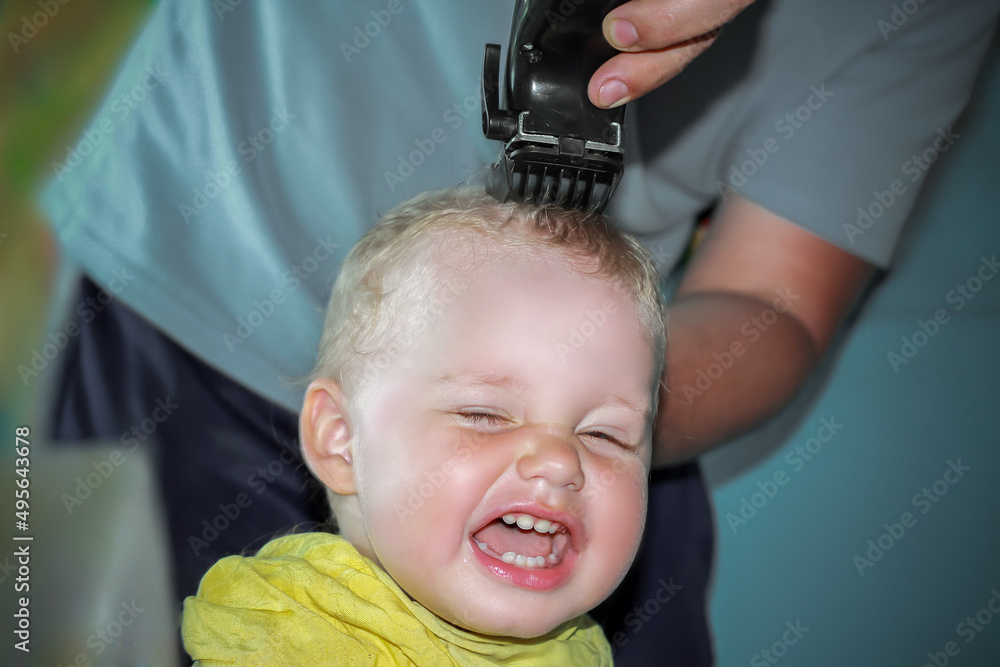 The first haircut on the head of a little boy in his life. A man is a father who cuts his son's hair. Shave the curls off the baby's head with an electric razor The first haircut on the head of a little boy in his life. A man is a father who cuts his son's hair. Shave the curls off the baby's head with an electric razor