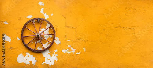 stare koło od wozu powieszone na żółtej obdrapanej z farby starej ścianie
