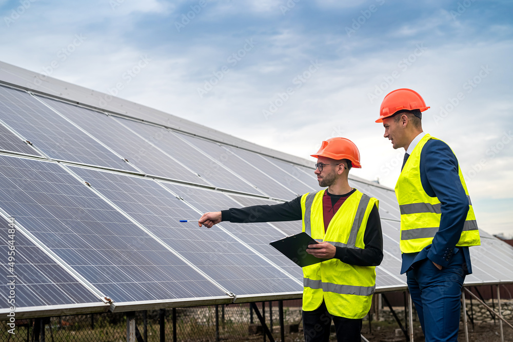 two young workers in overalls and helmets check the installed solar panels. two young workers in overalls and helmets check the installed solar panels.