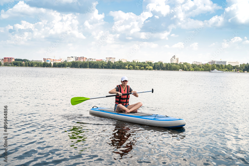 beautiful young woman in a protective vest learns to swim on a sup board on a city lake