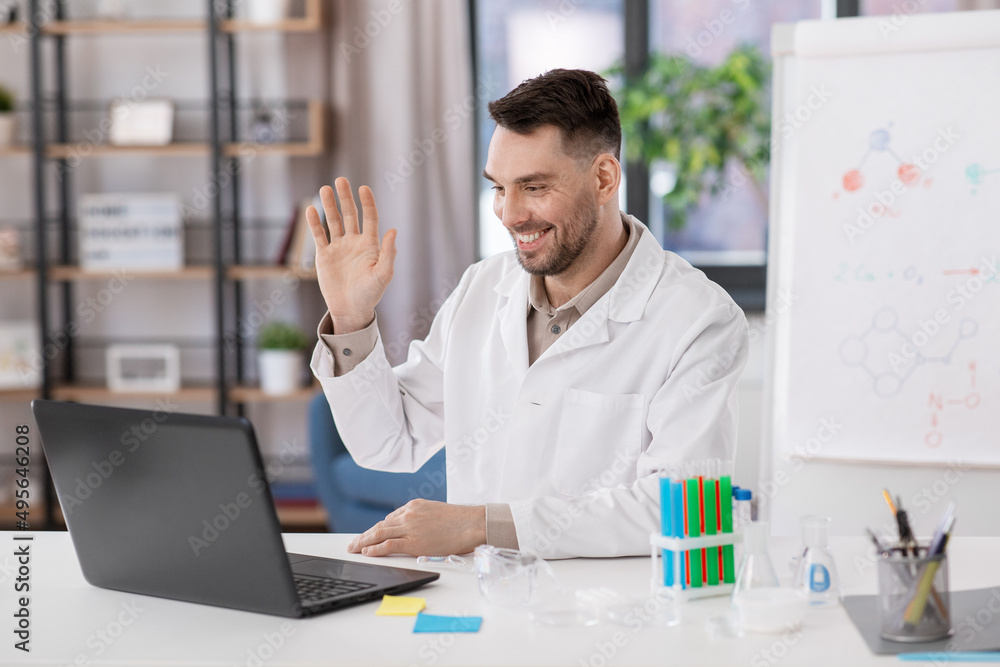 distant education, school and science concept - happy smiling male chemistry teacher with laptop computer having online class and waving hand at home office distant education, school and science concept - happy smiling male chemistry teacher with laptop computer having online class and waving hand at home office