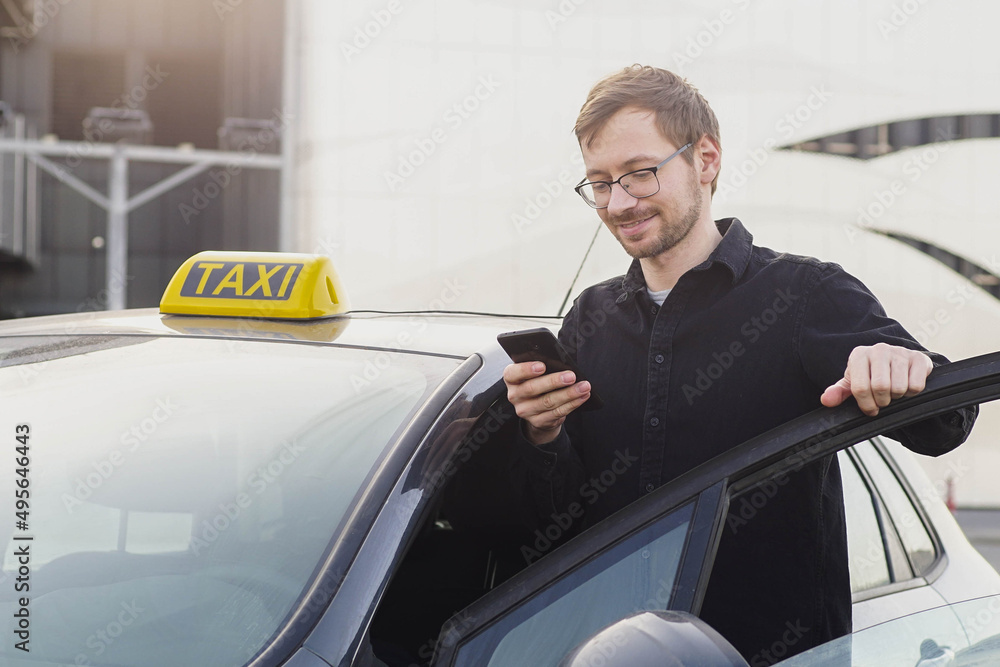 Portrait of smiling caucasian taxi driver standing near car and using smartphone. Portrait of smiling caucasian taxi driver standing near car and using smartphone.