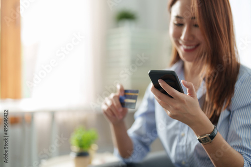 Young beautiful Asian woman using smartphone and credit card for online shopping at home with copy space. E-payment technology, shopaholic lifestyle, or mobile phone financial application concept