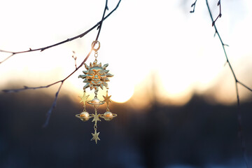 Solar golden amulet on branch, natural sunny blurred background. Sun symbol of spring equinox, winter solstice. winter or spring season 