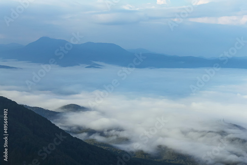 Morning in the mountains. A mountain gorge is covered with thick fog. Dark silhouettes of ridges and cloudy sky in the background. Beautiful landscape with fog.