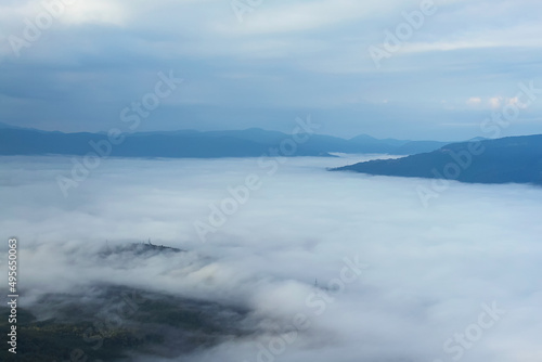 The hollow is covered with fog. In the background are mountain ranges and a cloudy sky. Beautiful landscape with fog.