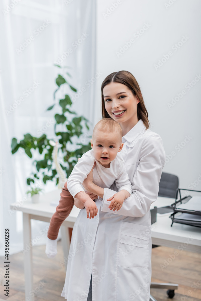 Cheerful family doctor holding baby in hospital. Cheerful family doctor holding baby in hospital.