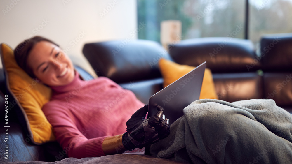 Woman With Prosthetic Arm Using Laptop Relaxing On Sofa At Home Woman With Prosthetic Arm Using Laptop Relaxing On Sofa At Home