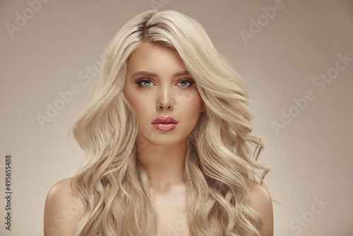 Beauty portrait of caucasian woman with blonde curly hair on beige isolated