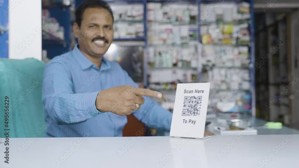 handheld rack foucs shot of Smiling pharmacist showing scan here to pay qr code for payment by looking at camera at store - concept of online payment, small business and technology. handheld rack foucs shot of Smiling pharmacist showing scan here to pay qr code for payment by looking at camera at store - concept of online payment, small business and technology.
