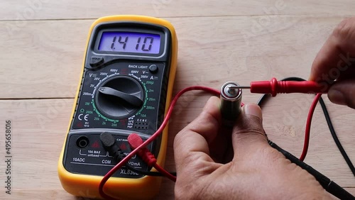 Hands are using a digital multimeter to measure electric voltage for checking battery cell 1.5 VDC on wooden background closeup.  photo