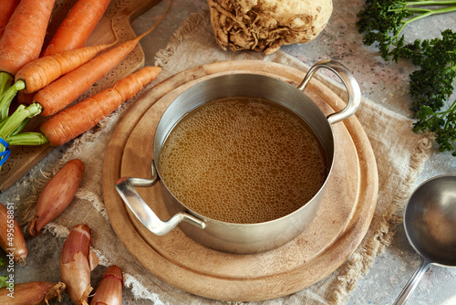 Tableau sur toile Bone broth or soup in a metal pot, with fresh vegetables