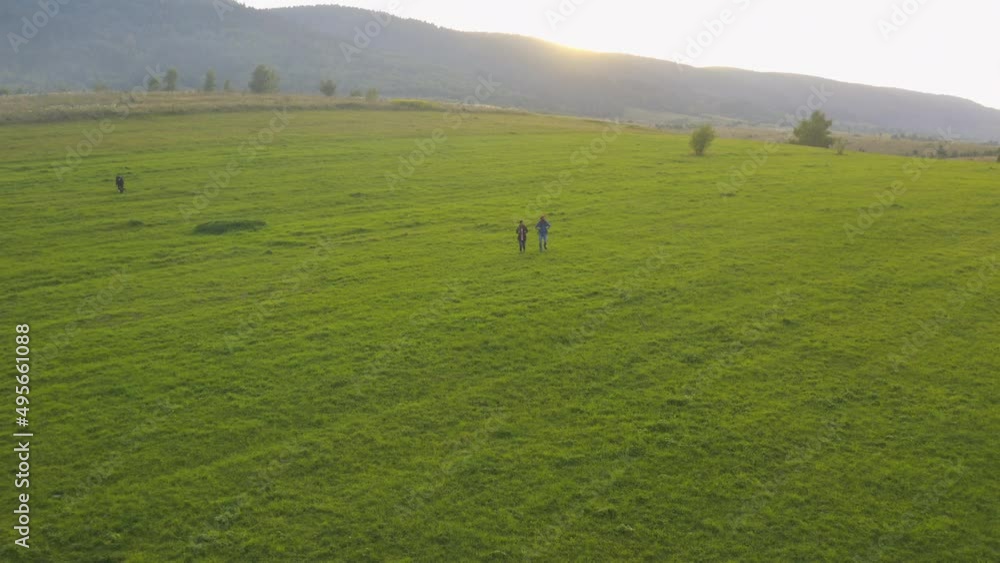 Aerial shot of happy multi-ethnic couple of friends wearing tourist backpacks hiking in beautiful nature. Farm animals herd grazing on field. Countryside hills. Summer trip. Aerial shot of happy multi-ethnic couple of friends wearing tourist backpacks hiking in beautiful nature. Farm animals herd grazing on field. Countryside hills. Summer trip.