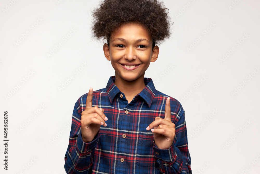 Number one. Indoor image of cute adorable dark-skinned child with stylish afro haircut putting index fingers up, being best of the best, lucky boy or winner, feeling happy, smiling at camera Number one. Indoor image of cute adorable dark-skinned child with stylish afro haircut putting index fingers up, being best of the best, lucky boy or winner, feeling happy, smiling at camera