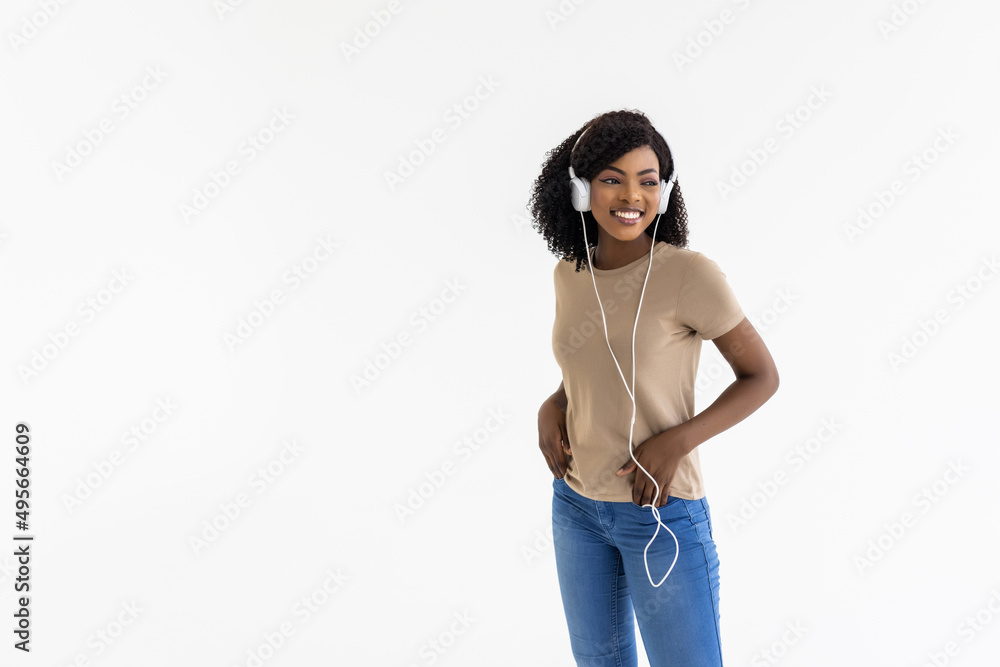Young african woman wearing headphones dancing active isolated on white wall listening to music l
