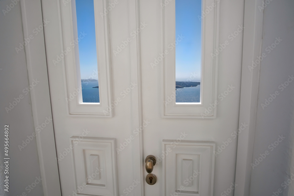 Fototapeta premium A typical white traditional door, the blue sky , the aegean sea and the volcano of Santorini in the background
