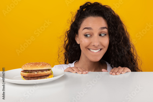 Slika na platnu Hungry Lady Looking At Burger Peeping Out Table