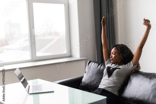 Happy relaxed african female worker student satisfied with finished work study at workplace. Carefree black lady holding hands behind head taking break after job well done enjoy no stress free relief photo