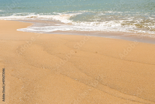 Blue sea waves with foam on yellow sand beach.