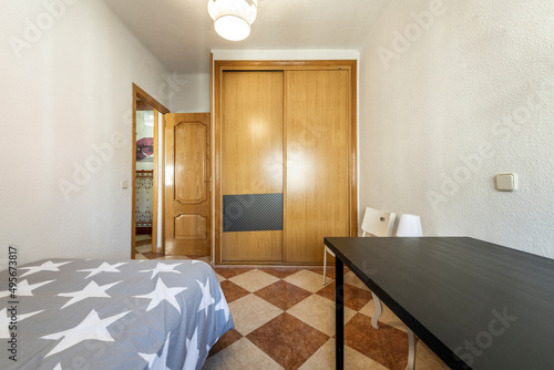 Youth bedroom with two-body built-in wardrobe  gray quilt with stars  black wooden desk and stoneware floors