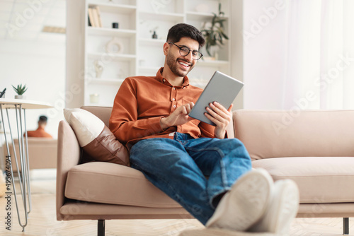 Smiling young Arab man using digital tablet at home photo